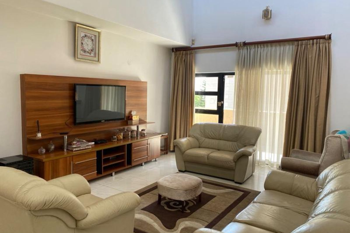 Spacious living room featuring high ceilings, tiled flooring, and a built-in wooden media console with direct access to an outdoor patio area.