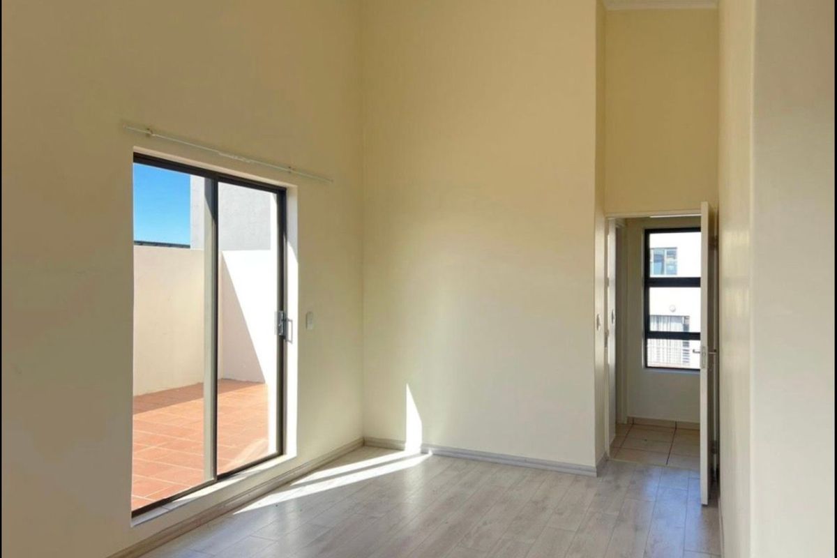 A bright, empty bedroom featuring light-toned laminate flooring, high ceilings, and a sliding glass door providing direct access to an outdoor balcony area.