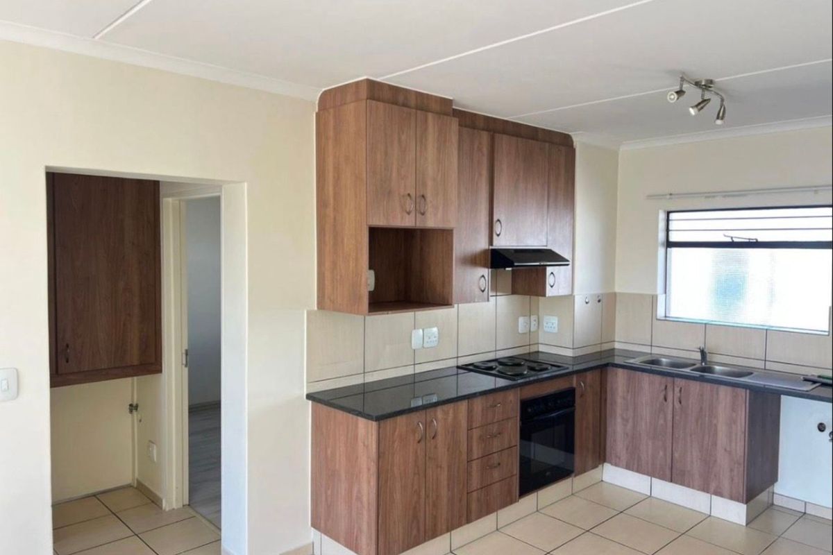 A functional kitchen featuring wood-look cabinetry, dark granite countertops, a built-in oven, hob, extractor fan, and tiled flooring.