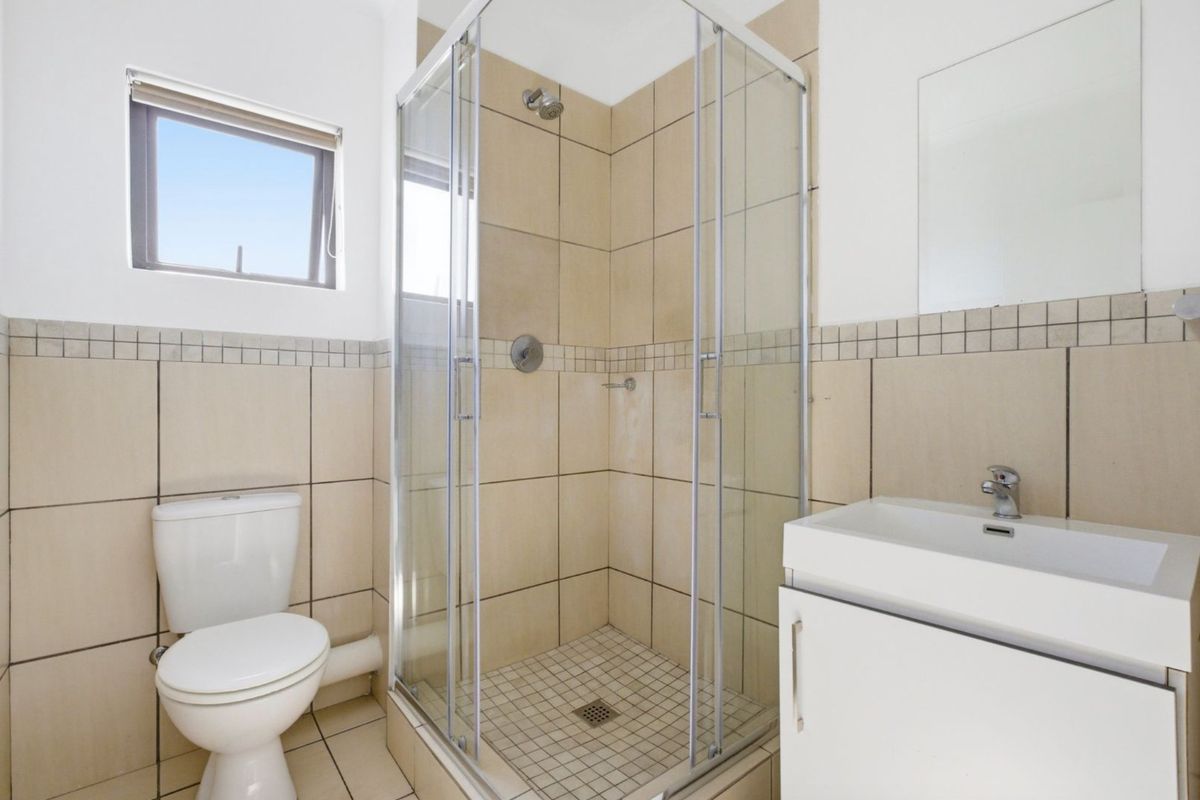 A functional bathroom featuring a glass-enclosed shower, a wall-mounted vanity with basin, and a standard toilet with tiled walls and flooring.