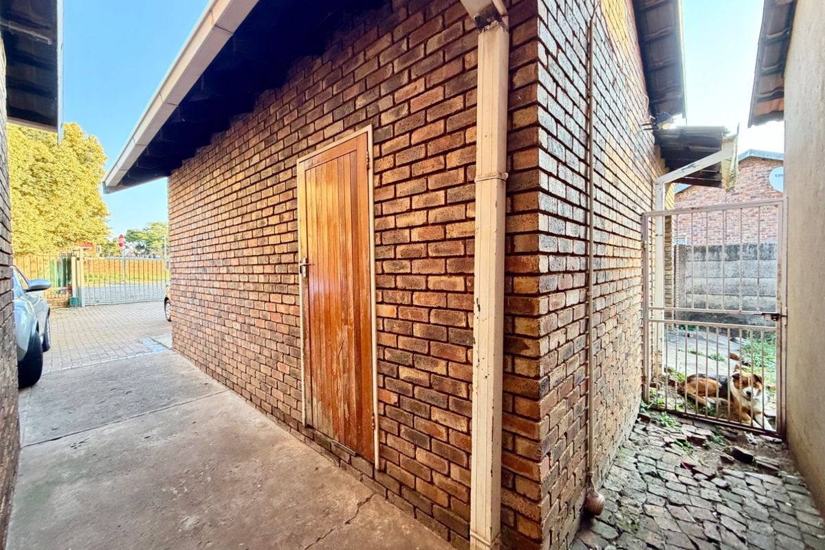 Exterior view of a brick outbuilding featuring a side access door, concrete pathway, and metal security gate.
