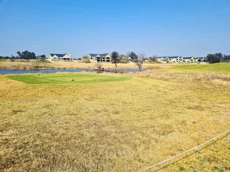 A scenic view of a residential estate featuring manicured lawns, a small lake, and surrounding multi-story homes in a peaceful setting.