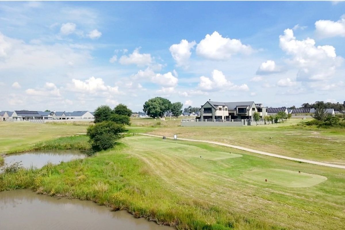 An elevated aerial view of a residential estate featuring a golf course, water feature, and surrounding modern homes.
