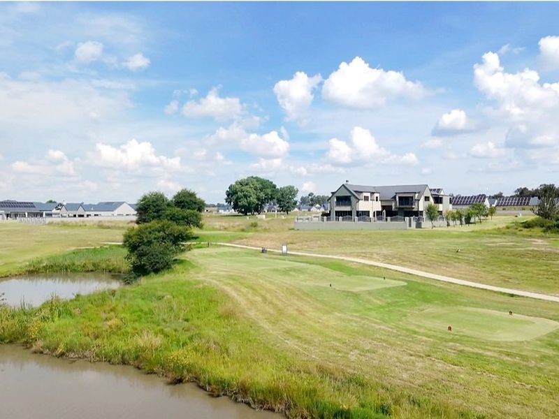 An elevated aerial view of a residential estate featuring a golf course, water feature, and surrounding modern homes.
