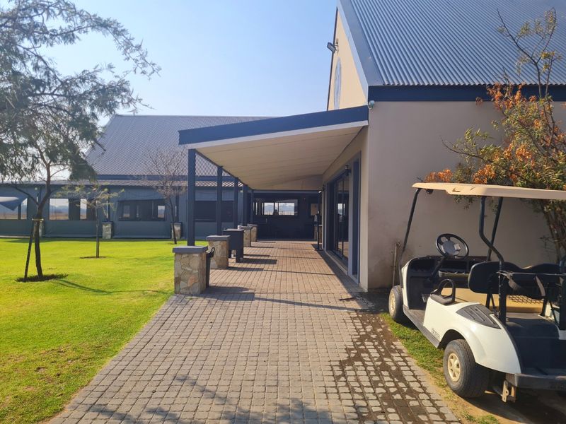 A covered paved patio area adjacent to a well-maintained building, featuring stone-clad pillars and a spacious lawn area.