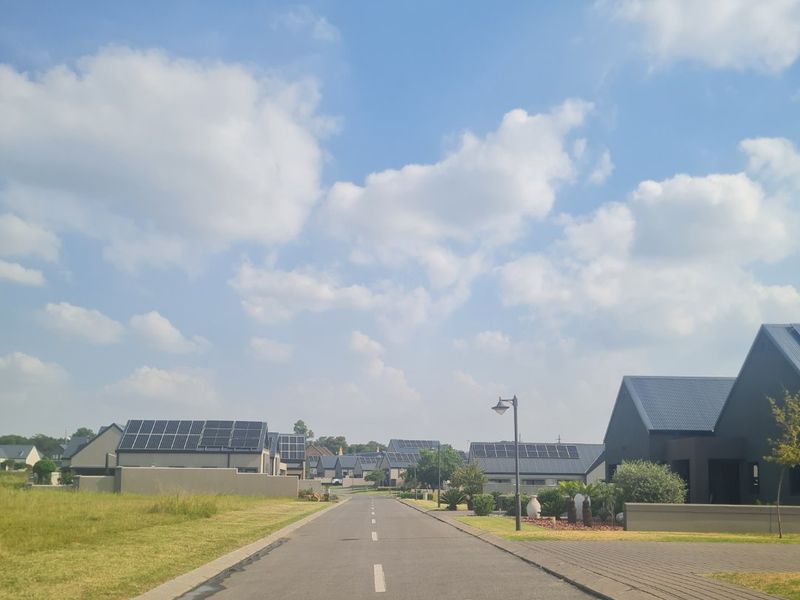 A view of a paved residential street within a modern estate, featuring surrounding homes with solar panel installations.