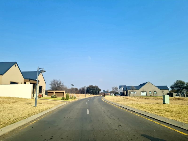 A view of a paved residential street within a developed estate, featuring surrounding modern homes and manicured grass verges.