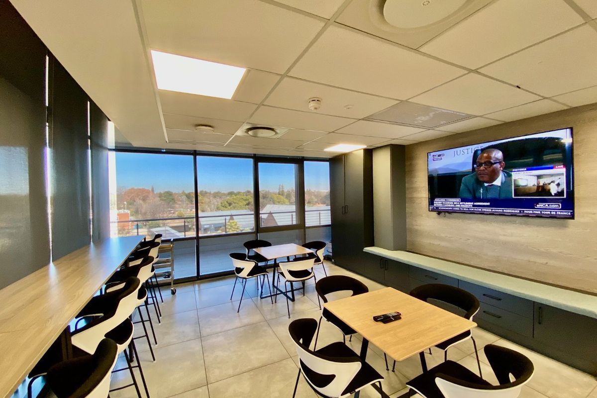 Modern commercial breakroom or breakout area featuring large windows, tiled flooring, built-in cabinetry, and wall-mounted television.