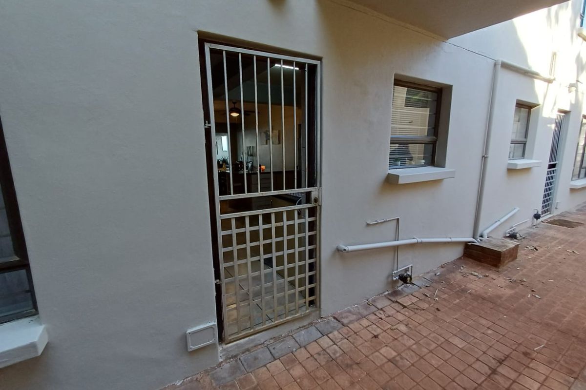 Exterior view of an apartment entrance featuring a security gate, tiled walkway, and visible exterior plumbing fixtures.