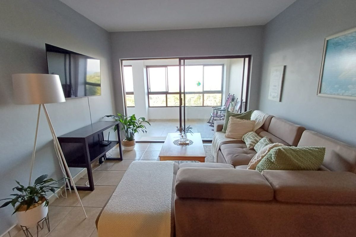 A comfortable living room featuring tiled flooring and large sliding glass doors that open onto a private balcony, providing natural light and outdoor access.