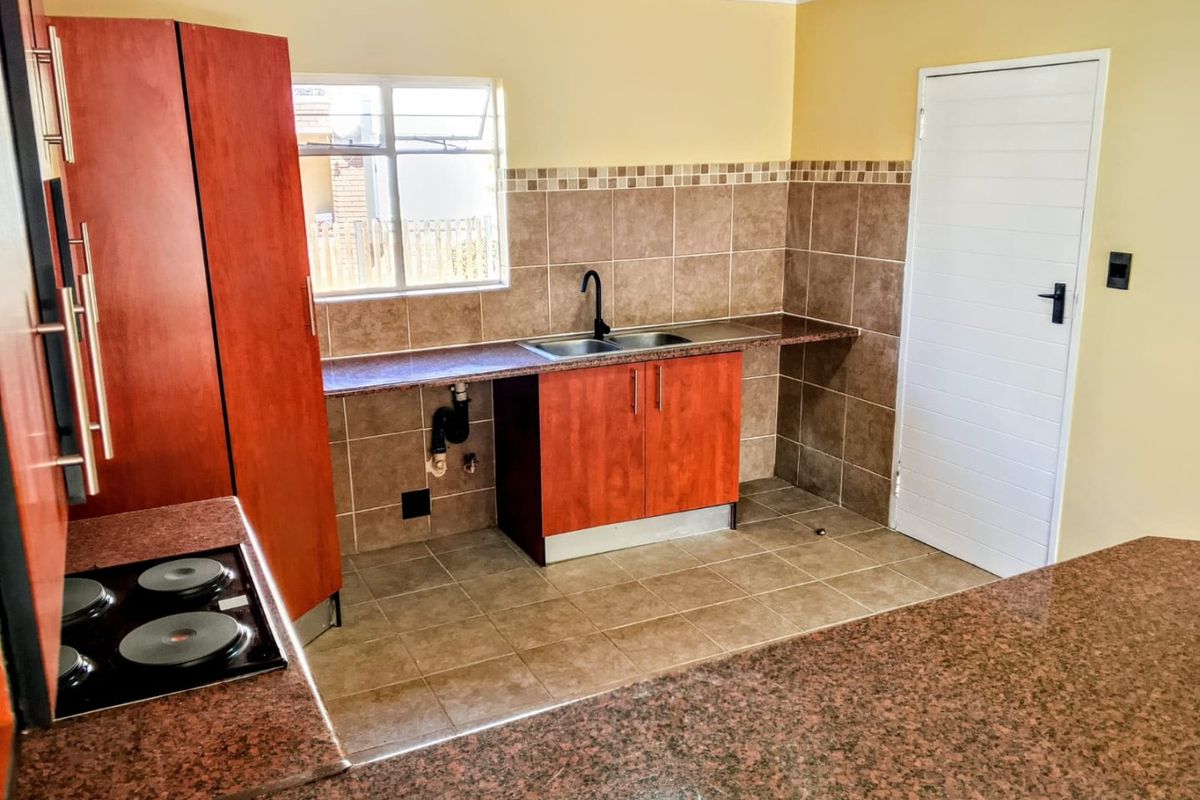 A functional kitchen featuring cherry-wood cabinetry, granite countertops, a built-in electric hob, and tiled splashbacks with a double sink.