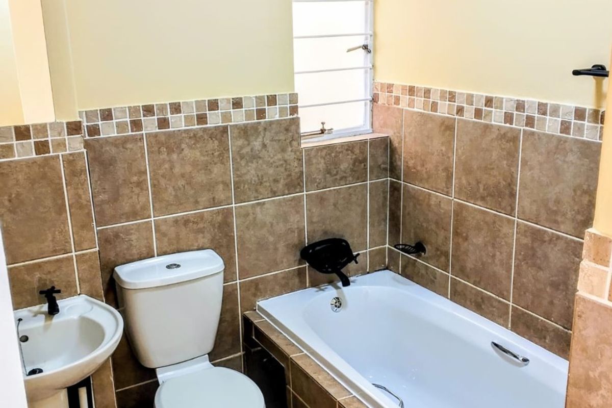 A functional bathroom featuring a pedestal basin, toilet, and a tiled bathtub surround with a window for natural light.