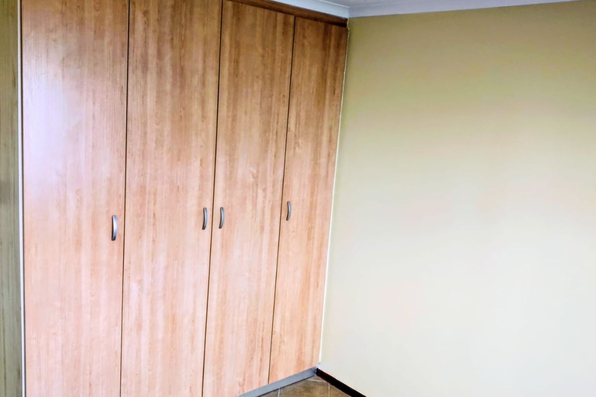 A bedroom featuring built-in wooden cabinetry with modern handles and tiled flooring.