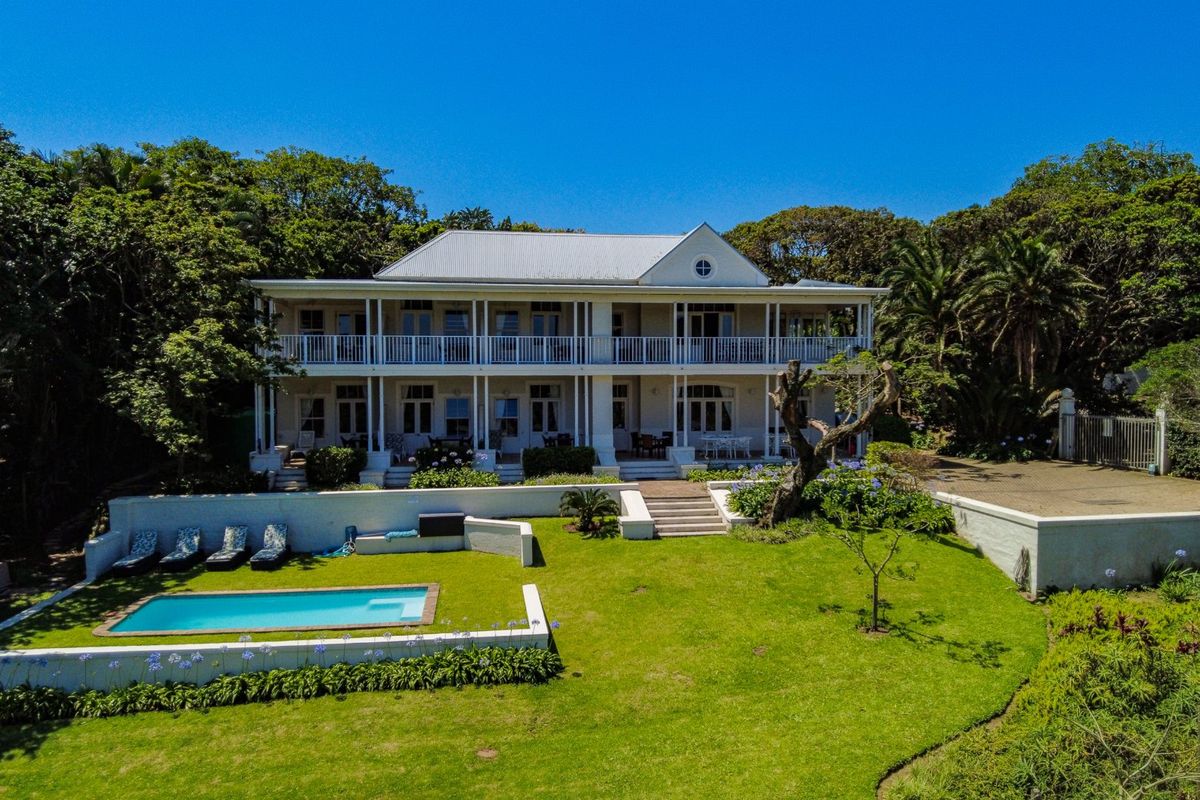 Aerial view of a grand two-story residence featuring a wrap-around veranda, swimming pool, and expansive landscaped garden.