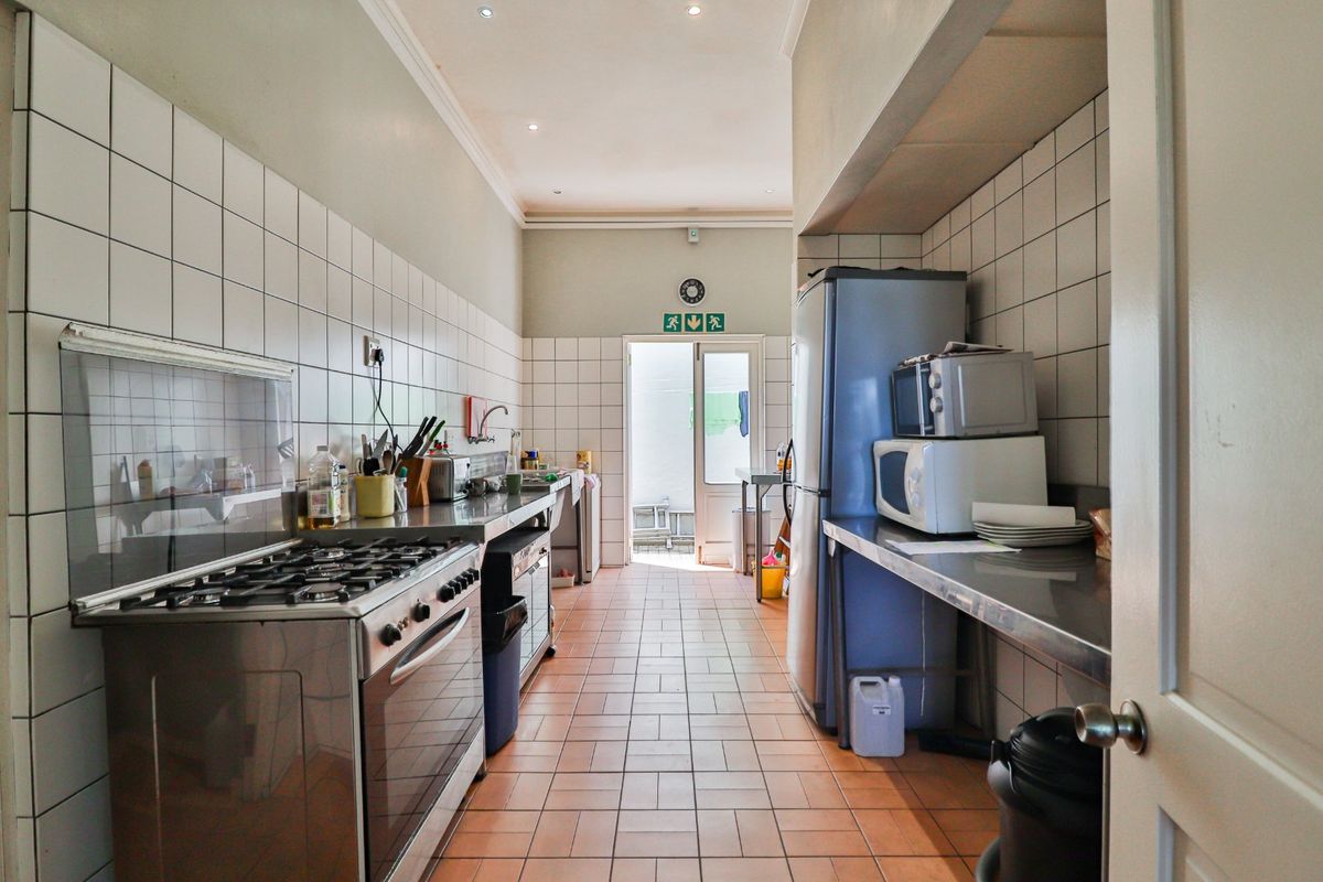 A functional galley-style kitchen featuring stainless steel countertops, tiled walls, and a gas stove, leading directly to an outdoor area.