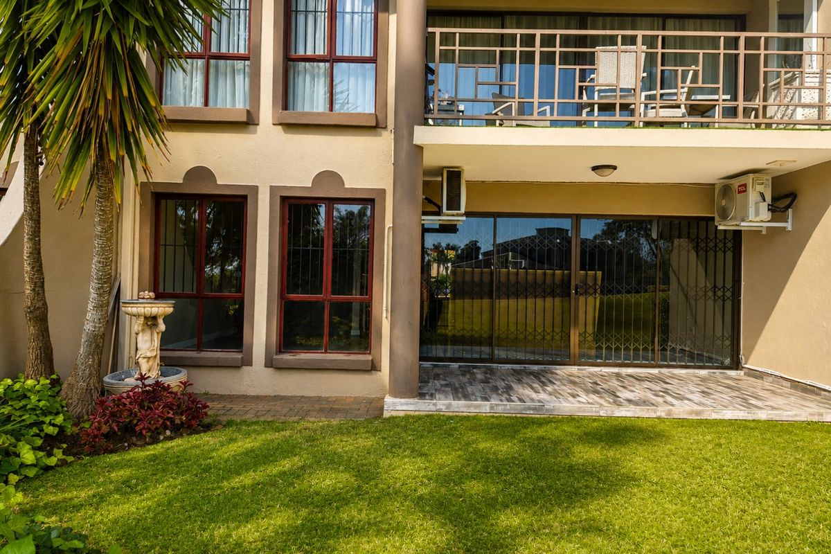 Rear view of the apartment featuring a ground floor patio with tiled flooring, a first-floor balcony, and a well-maintained garden area.