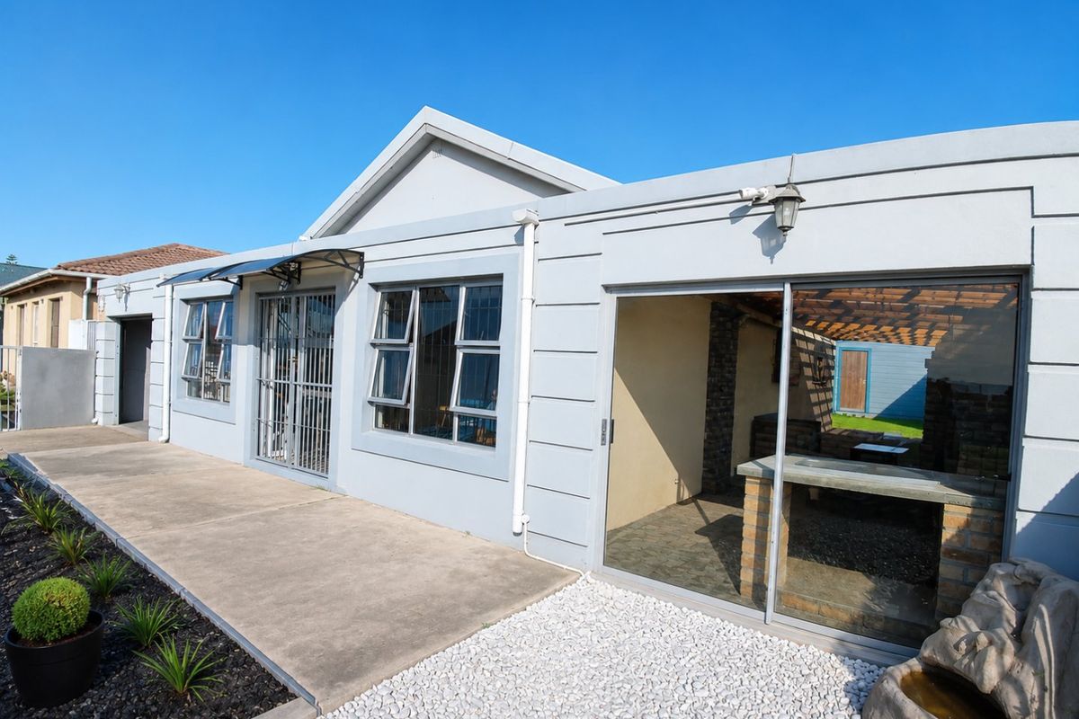 Rear exterior view of the house featuring a paved patio area, sliding glass doors, and a built-in outdoor braai or entertainment space.