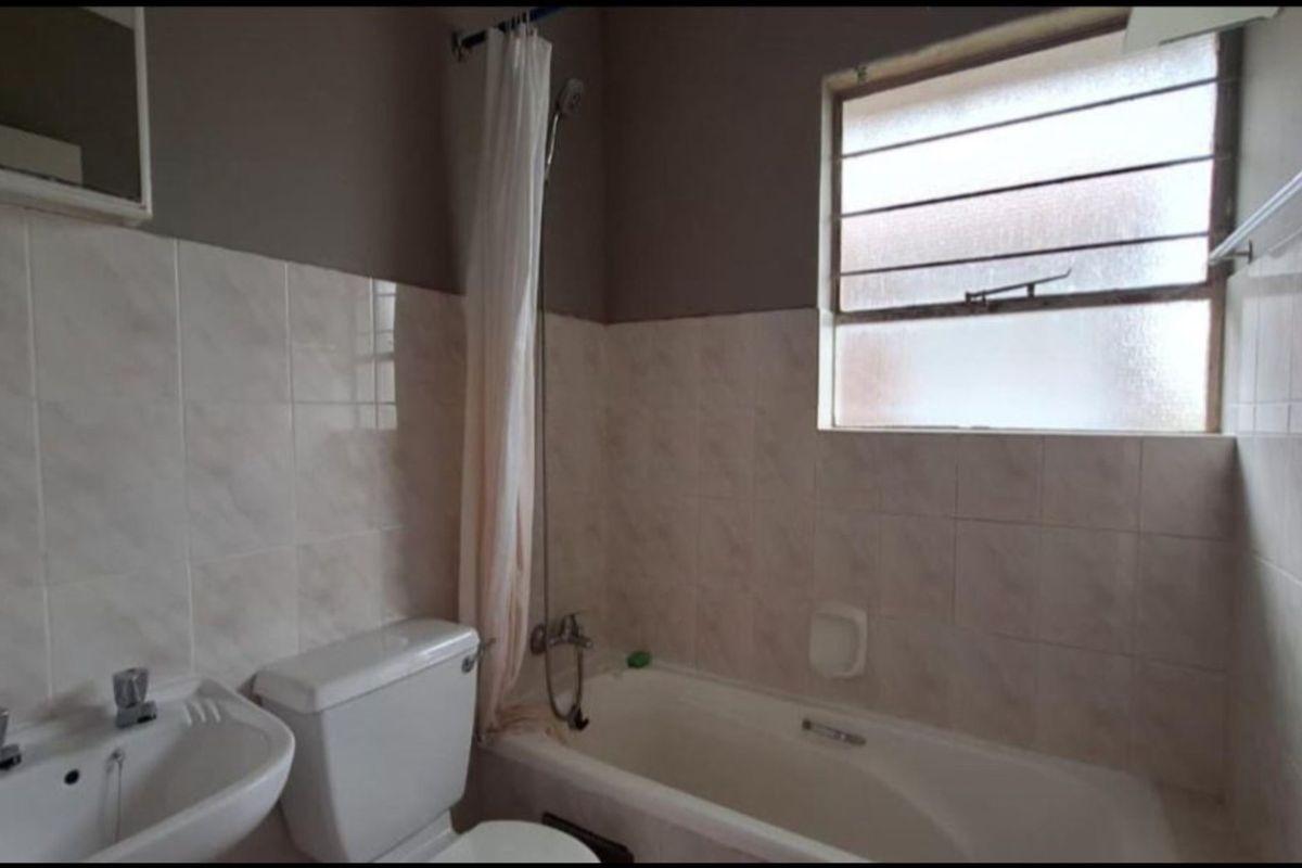 A functional bathroom featuring a standard bathtub with shower attachment, a pedestal basin, and a window with security bars.