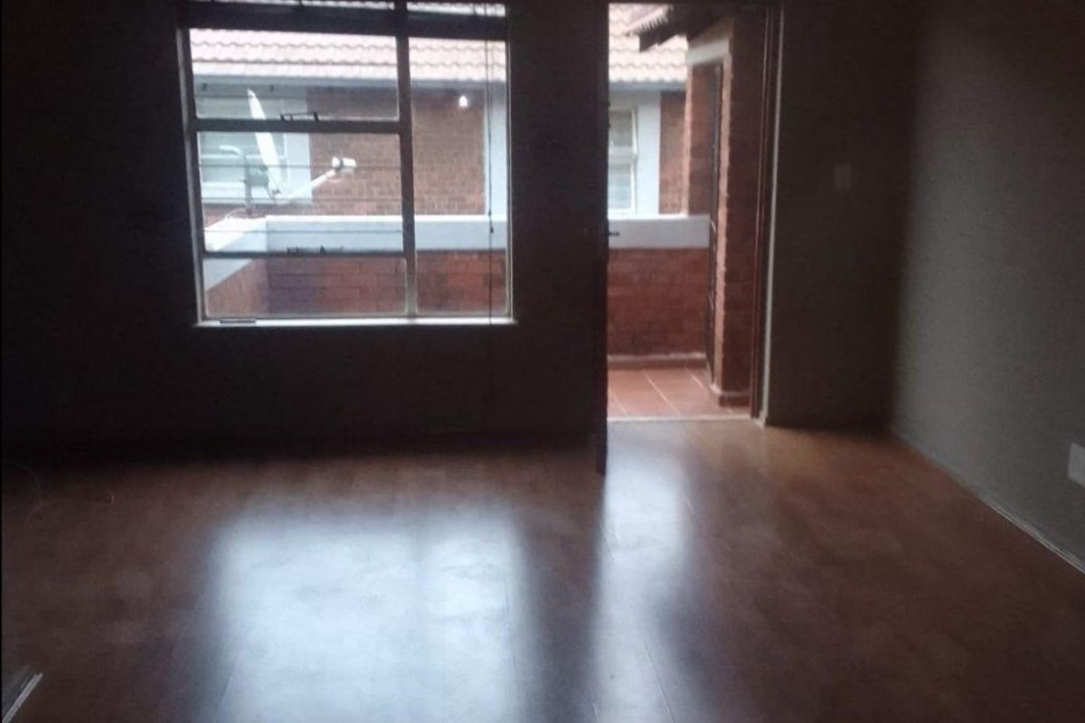 An empty living room featuring laminate flooring, a large window, and direct access to an outdoor balcony area.