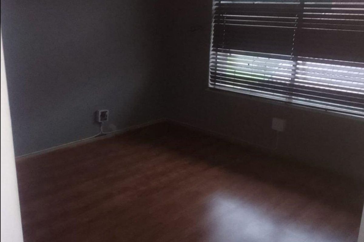 A vacant bedroom featuring dark wood-look laminate flooring and fitted window blinds, offering a neutral blank canvas for personalization.