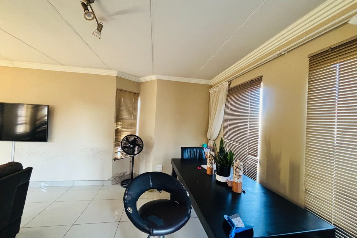 A living area featuring tiled flooring, crown molding, and multiple windows fitted with venetian blinds.