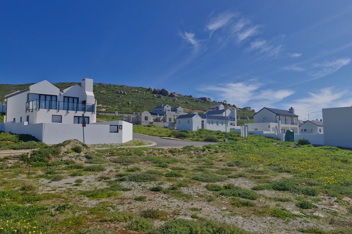 A view of a residential estate featuring vacant land in the foreground with established modern homes and coastal landscape in the background.