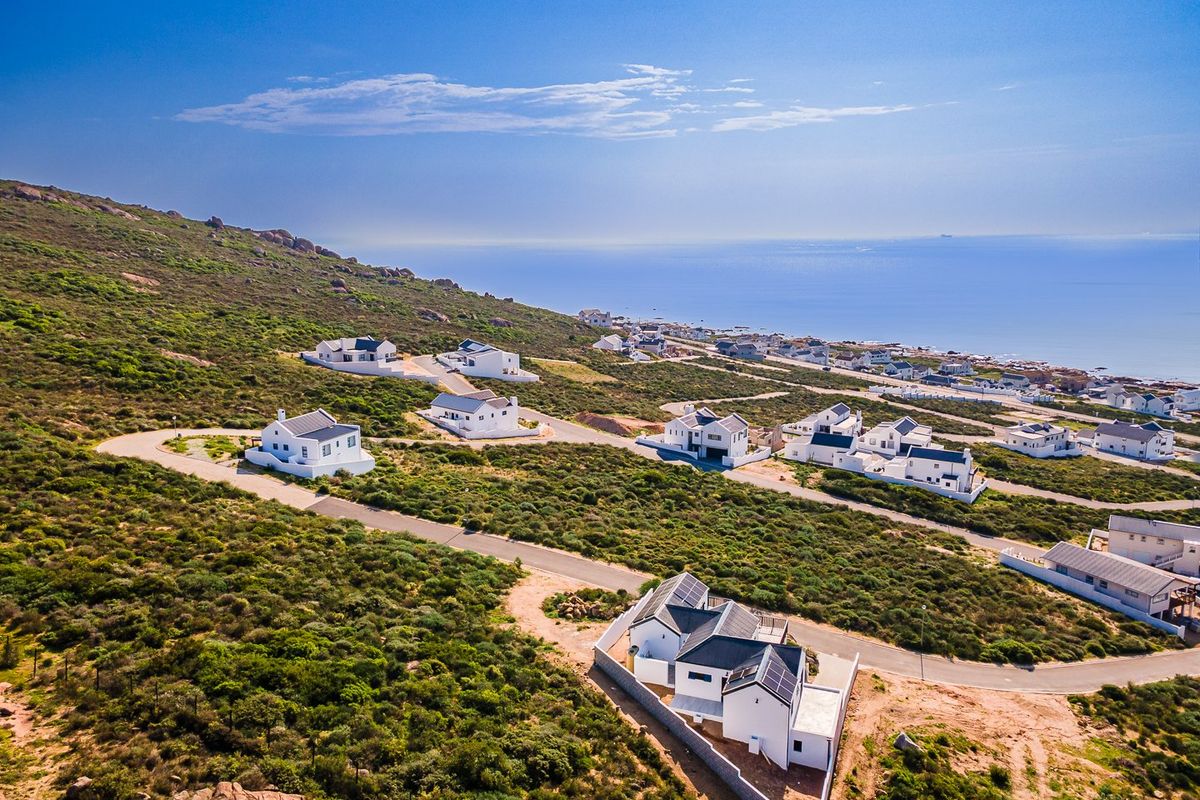Aerial view of a coastal residential estate featuring modern white homes with dark roofs, winding paved roads, and scenic ocean views.