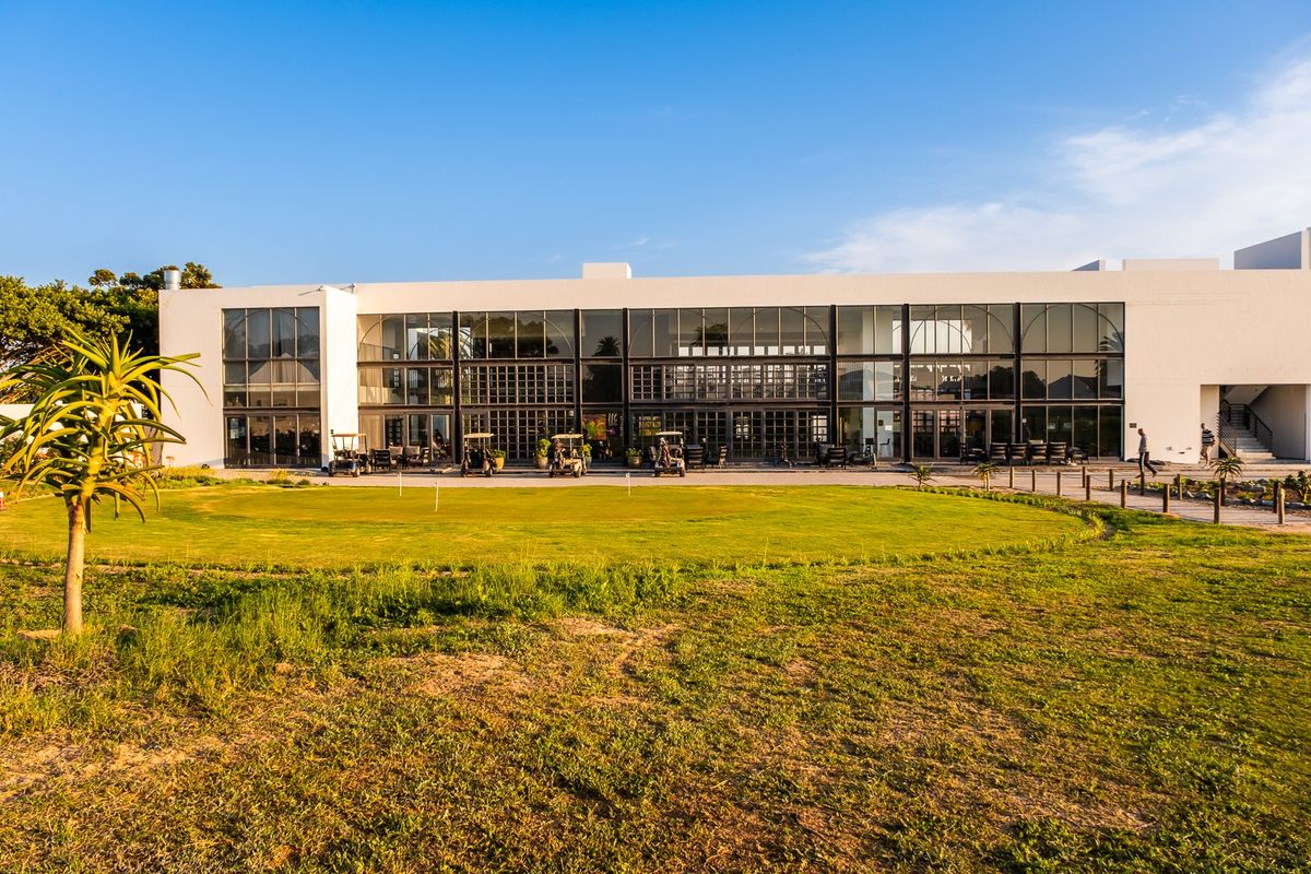 A modern clubhouse building featuring expansive floor-to-ceiling glass facades, overlooking a manicured lawn and golf course area.