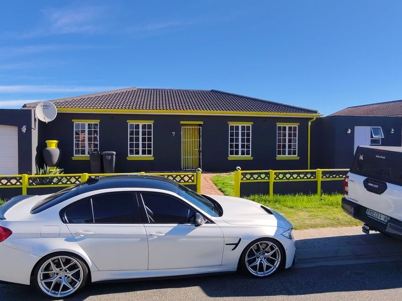 Front exterior view of a single-story residential house featuring a dark facade with contrasting yellow trim, tiled roof, and a secure perimeter fence.