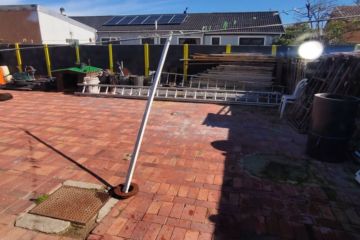 A paved rear outdoor area featuring a perimeter wall and a central metal washing line pole.