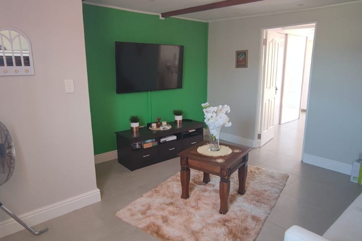 A living room featuring tiled flooring, a green accent wall, and recessed ceiling lighting, providing a functional and bright living space.