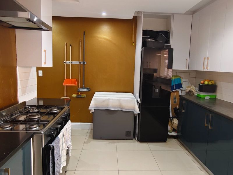 Modern kitchen featuring two-tone cabinetry, dark stone countertops, a gas hob with extractor fan, and tiled flooring.