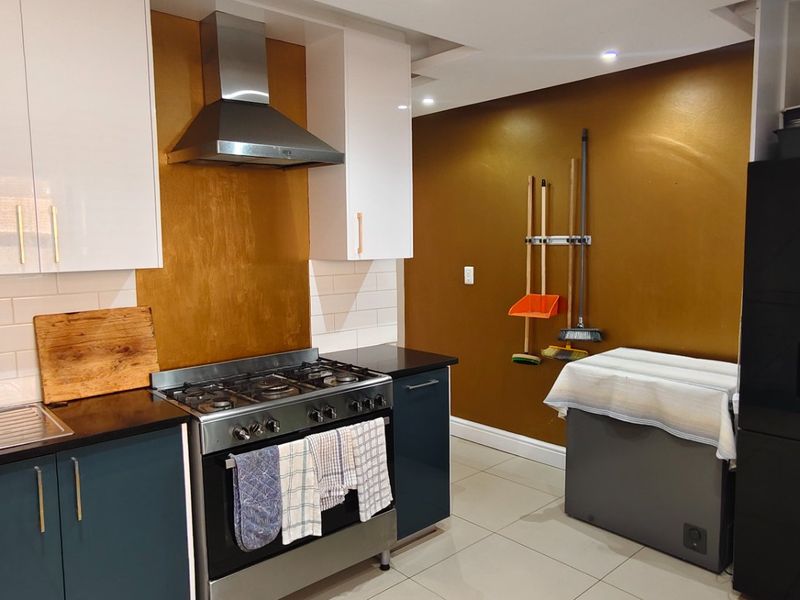 Modern kitchen featuring high-gloss cabinetry, a stainless steel gas stove with extractor fan, subway tile backsplash, and tiled flooring.