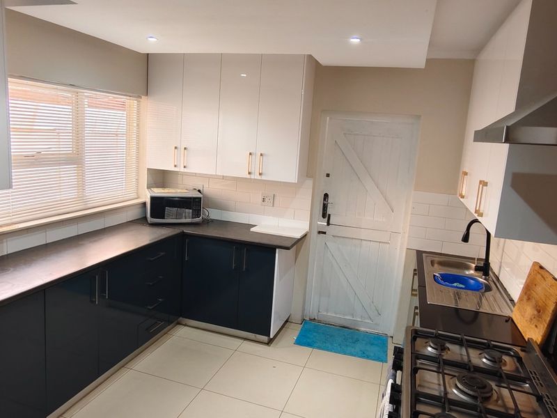 Modern kitchen featuring high-gloss cabinetry, dark countertops, built-in gas hob, extractor fan, and tiled flooring with ample storage space.
