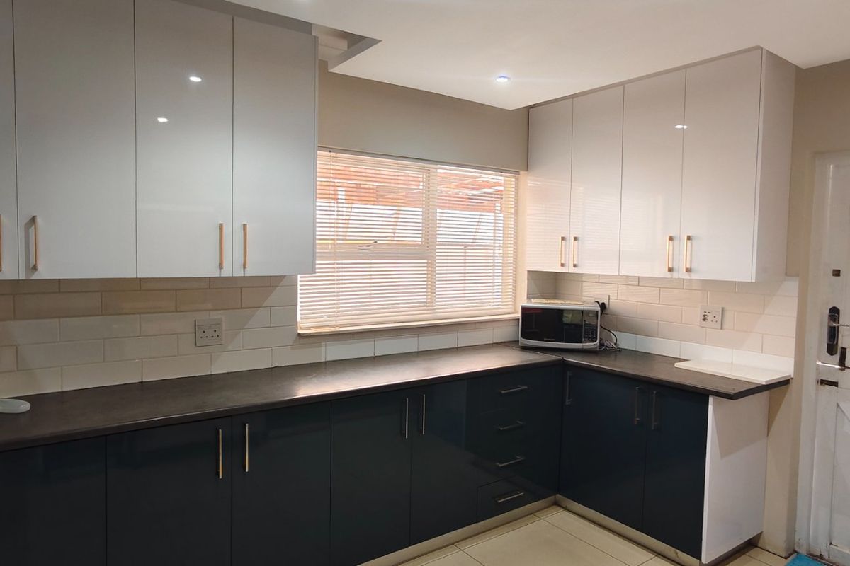 Modern kitchen featuring high-gloss cabinetry, dark countertops, subway tile backsplash, and a functional layout with integrated storage and natural light.