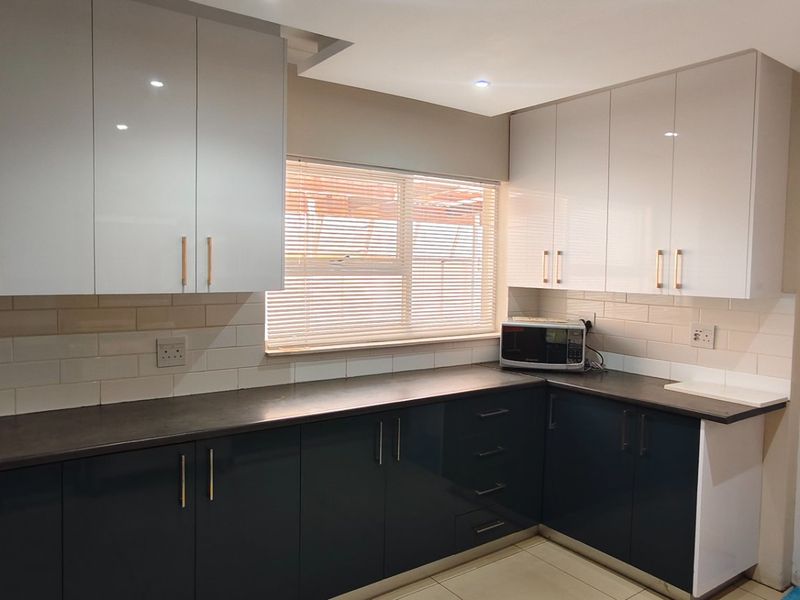 Modern kitchen featuring high-gloss cabinetry, dark countertops, subway tile backsplash, and a functional layout with integrated storage and natural light.