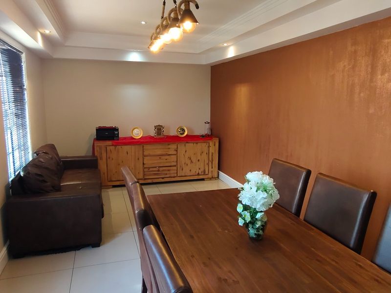 A well-maintained dining area featuring tiled flooring, recessed ceiling lighting, and a decorative feature wall.
