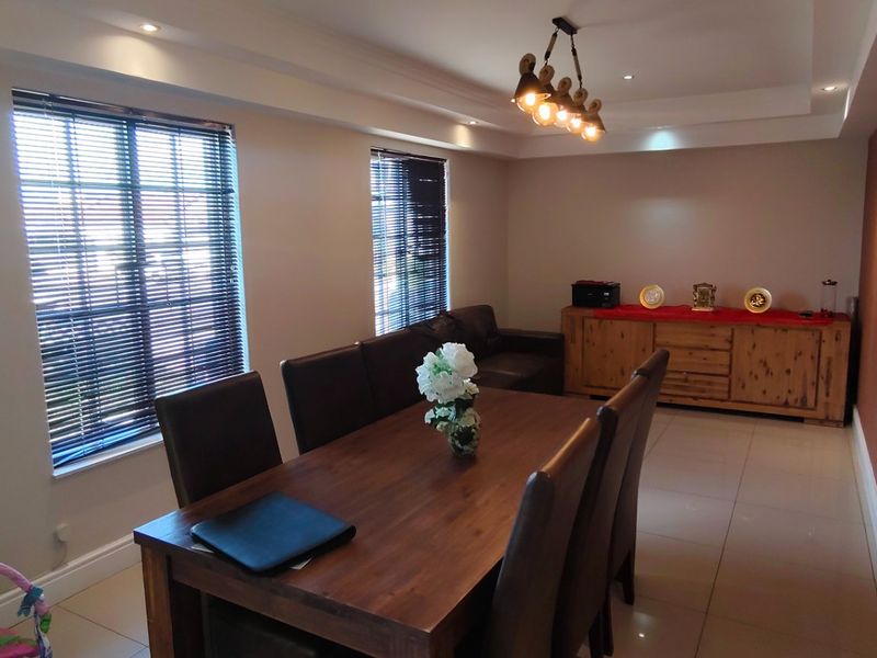 A spacious dining room featuring tiled flooring, recessed ceiling lighting, and large windows with fitted blinds, creating a bright and functional living space.