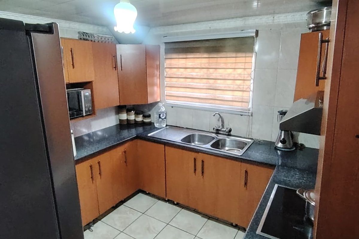 A functional kitchen featuring wood-tone cabinetry, dark granite countertops, a double-basin stainless steel sink, and a built-in electric cooktop.