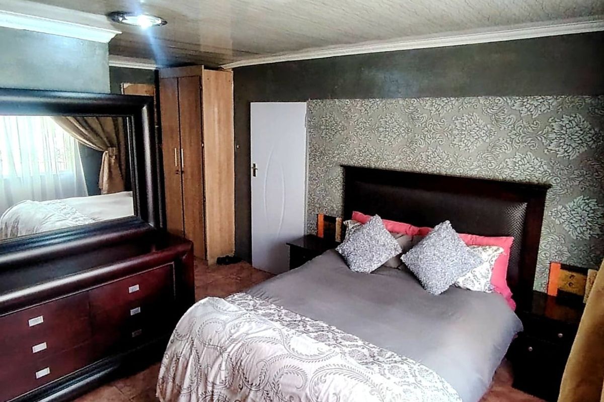 A bedroom featuring a built-in wardrobe, patterned wallpaper accent wall, and tiled flooring.