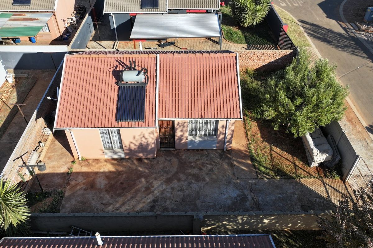 Aerial view of a residential property featuring a tiled roof, solar water heating system, and a paved driveway area with surrounding boundary walls.