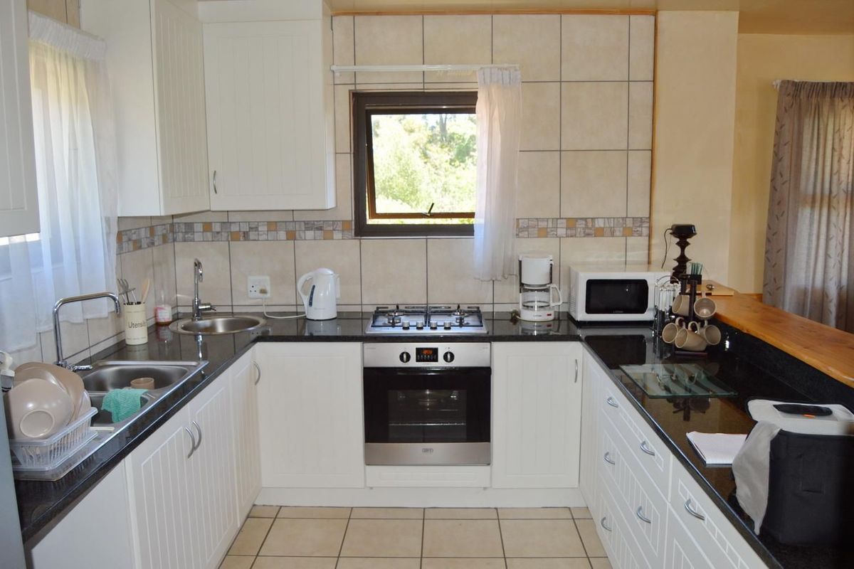 A functional kitchen featuring white cabinetry, dark granite countertops, a gas hob, built-in oven, and a breakfast bar with tiled backsplash.