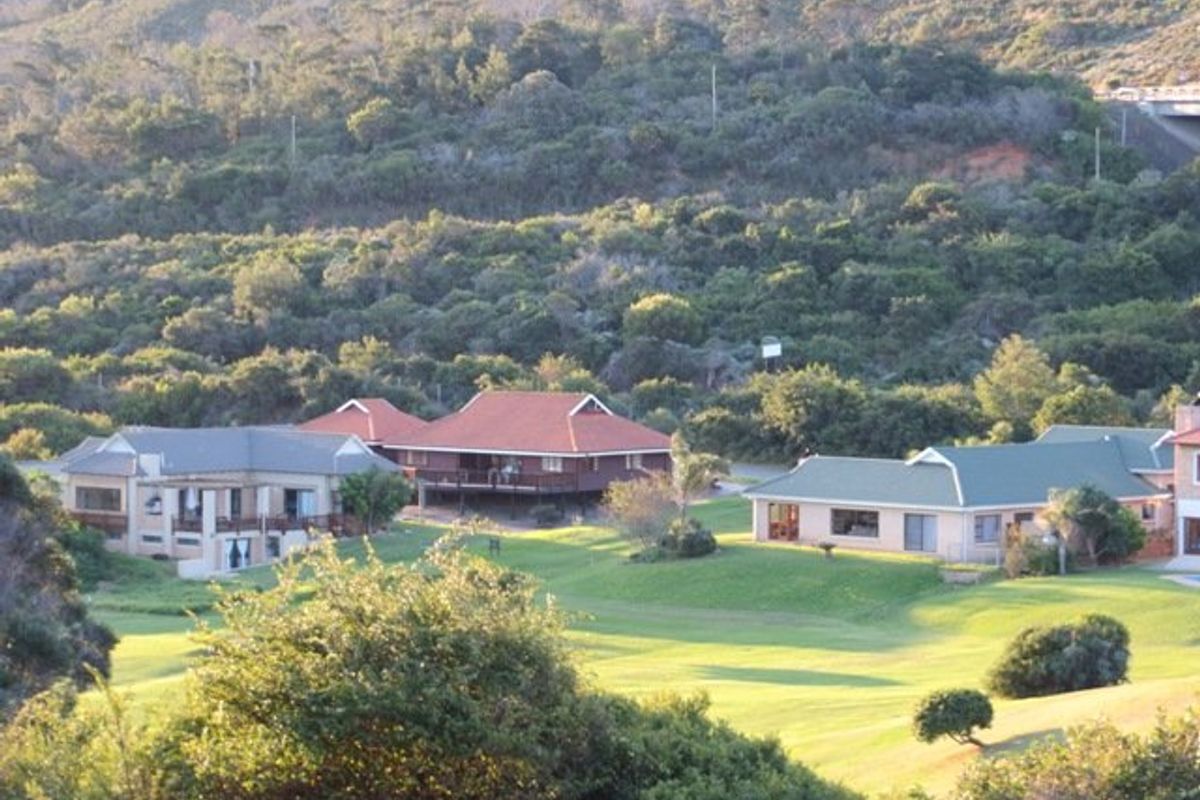 An elevated view of residential properties set within a lush, green landscape with rolling hills and mature trees in the background.