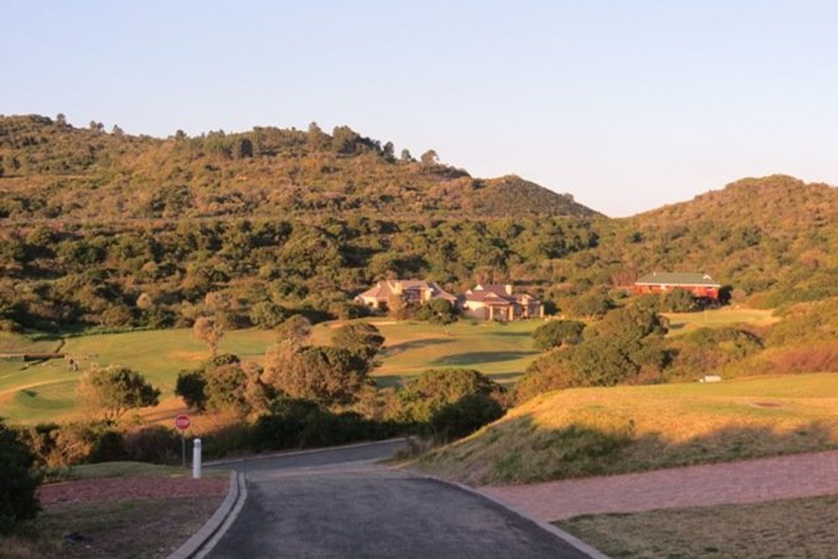 A scenic view of the residential estate featuring rolling hills, landscaped greenery, and distant houses viewed from an elevated road approach.