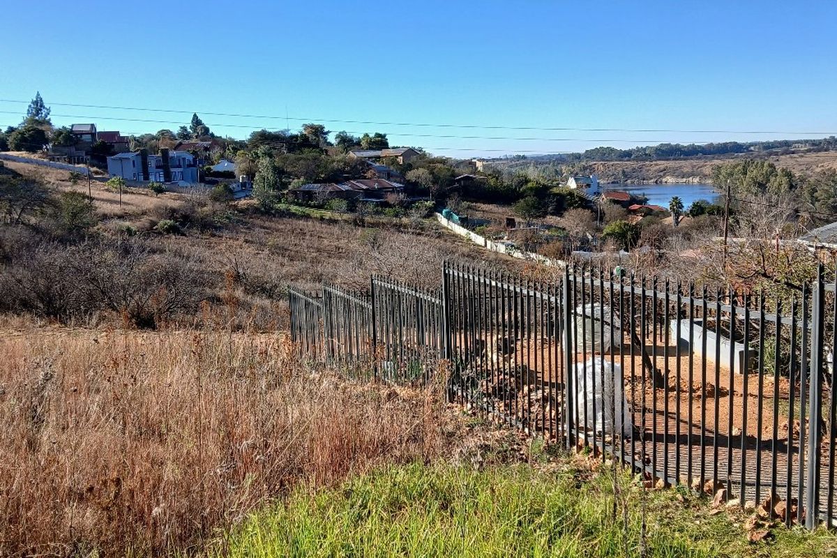 A view of the vacant residential land featuring a metal perimeter fence, overlooking the surrounding neighborhood and nearby water body.