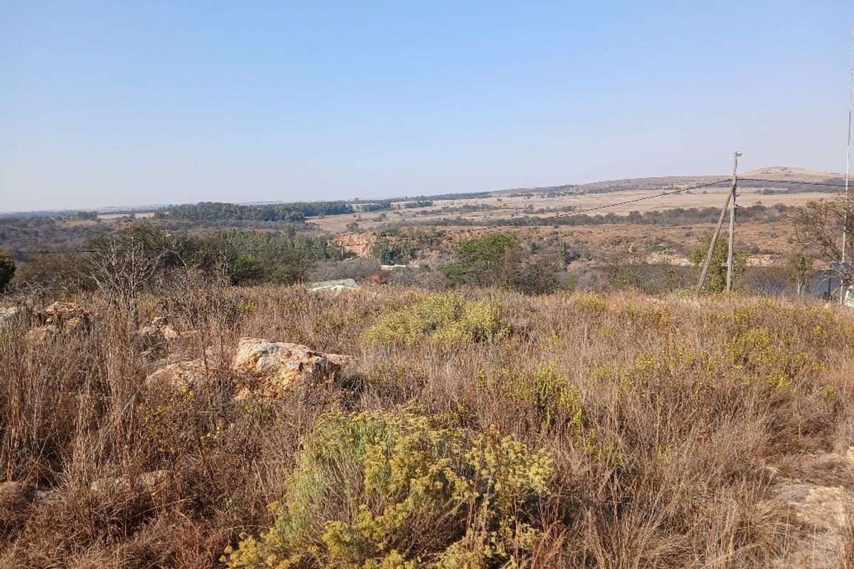 Expansive view over the natural landscape, featuring dry grassland, rocky outcrops, and distant rolling hills.