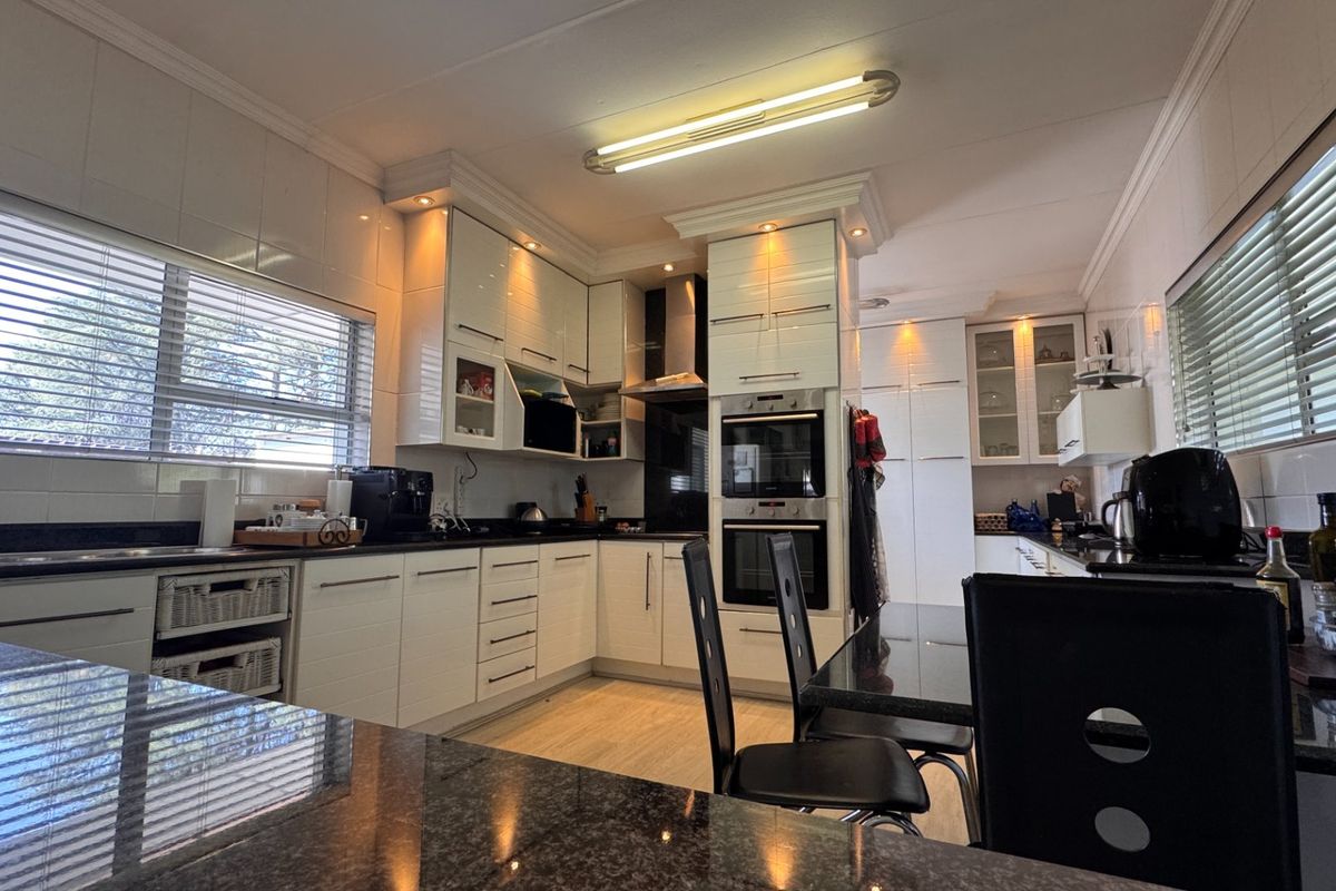 Modern kitchen featuring high-gloss cabinetry, granite countertops, built-in double oven, and integrated extractor fan with ample natural light from large windows.