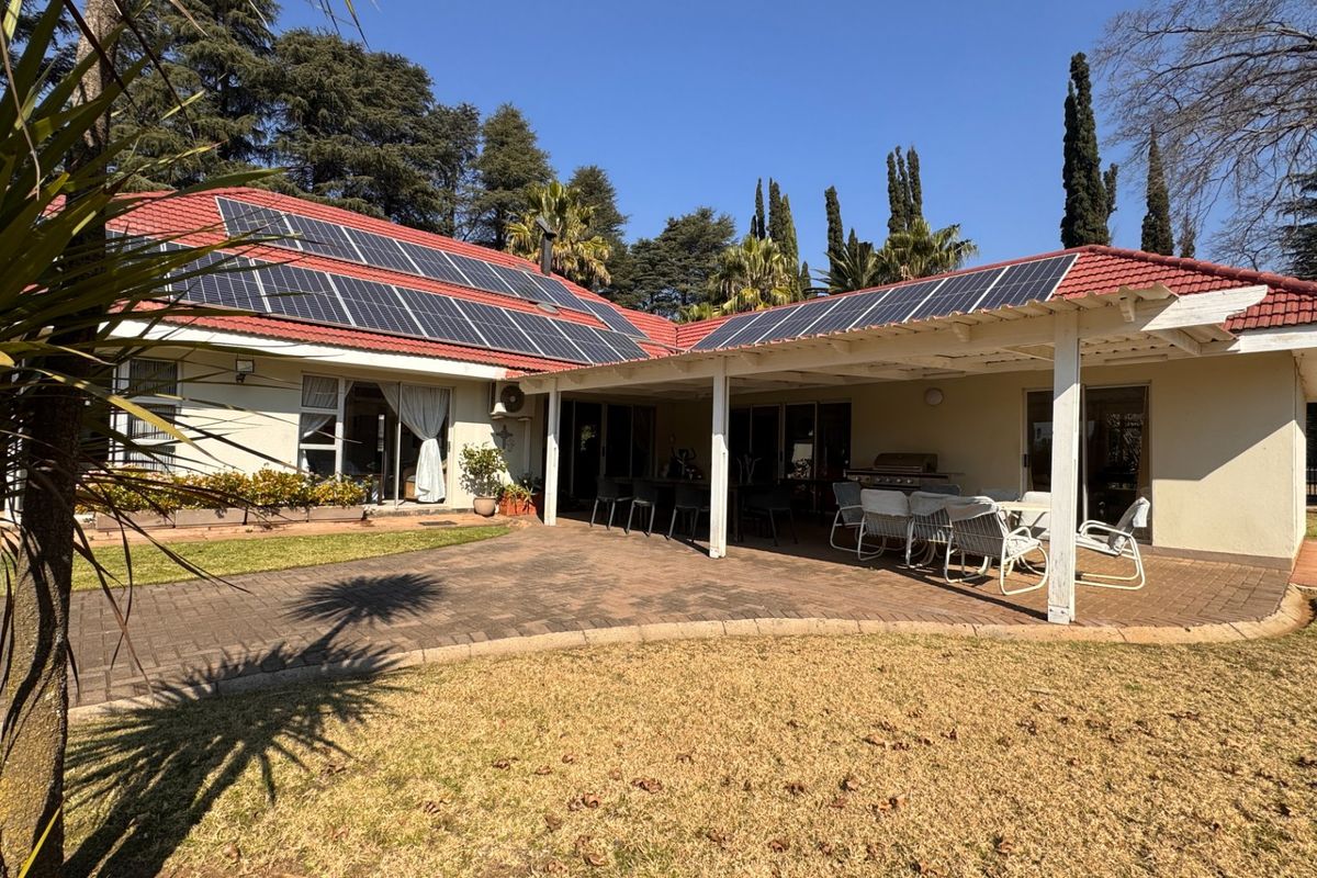 Spacious rear exterior featuring a covered patio area, paved courtyard, and a tiled roof equipped with a large solar panel array.