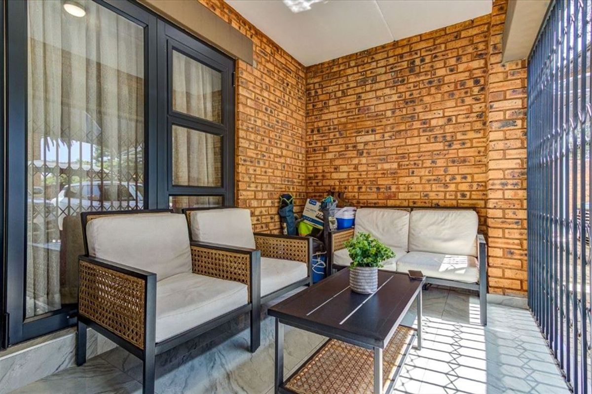 A covered patio area featuring exposed brick walls, tiled flooring, and secure metal security gates, providing a functional outdoor living space.
