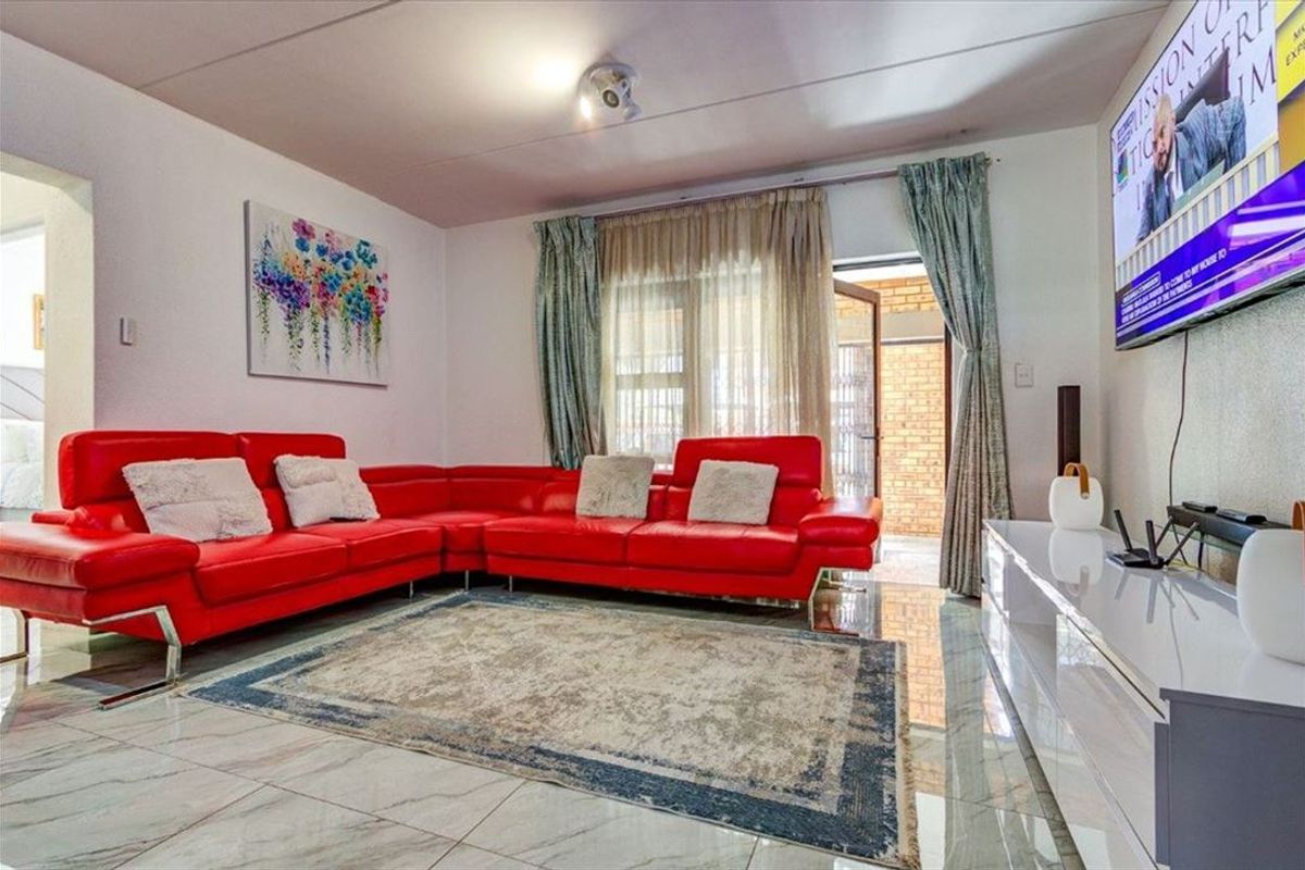 A bright living room featuring polished marble-look floor tiles, large windows with curtains, and direct access to an outdoor patio area.
